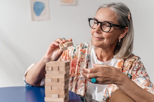 Elderly woman having fun with a Jenga puzzle indoors, wearing stylish eyewear.